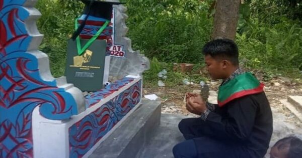 Pemuda Desa Rante Alang, Luwu bersimpuh dan berdoa di depan makam ayahnya, usai wisuda virtual UMI Makassar, Minggu (25/10/2020). foto:ig palopo_info